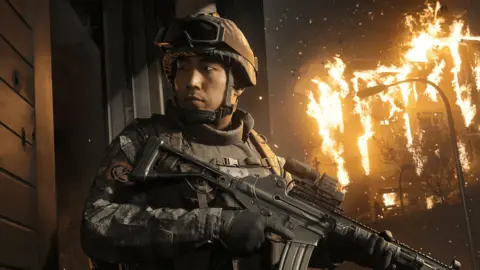 Infinity Ward / Activision An in-game screenshot showing a male Korean soldier holding a gun with a building on fire behind him.