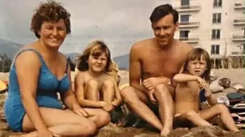 Family photo A colour photo of Jane Blackwell as a child on a beach with her sister, father and mother. 
