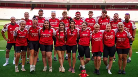 A group of people wearing arsenal t shirts posing pitch-side at the emirates stadium in London 