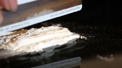 PA Media A person cutting up cocaine - only their hand can be seen, as well as the drug