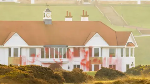 PA Media Red paint covering the front of the Trump Turnberry resort. The building is white with an orange roof. It has red paint covering part of the frontage and windows.