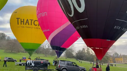 Three hot air balloons inflated at Ashton Court Estate in Bristol - launching the city's balloon fiesta.