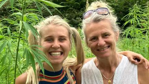 Kitty Wilson Brown and her business partner Claire O’Sullivan stand together smiling in the middle of a green, sunlit hemp crop  