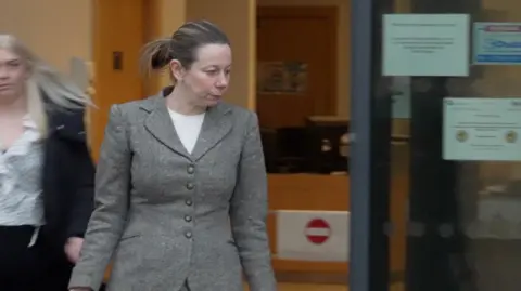 DJ McLaren/BBC Woman in grey suit and pony tail leaves court building