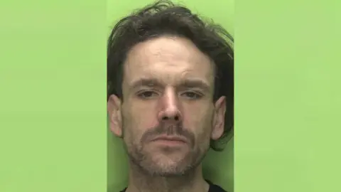 Nottinghamshire Police A headshot of Aaron Kelly, who has long dark hair, against a green background.