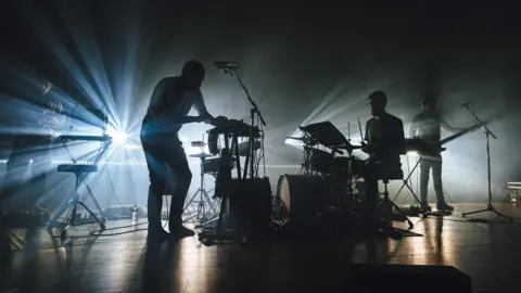 SoulMedia Members of the band Caribou are silhoutted by spotlights behind them as they perform on stage at Bristol Beacon