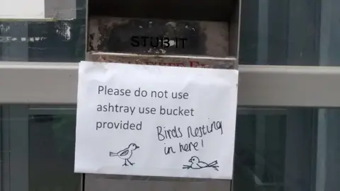 Mark Pointer Cigarette butt bin with bird nesting notice