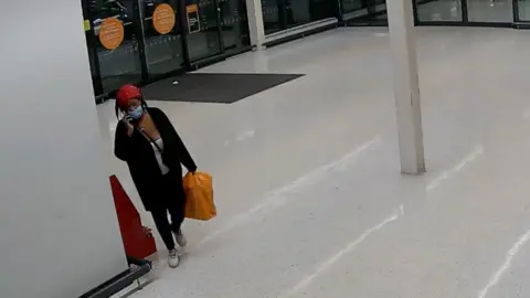 Metropolitan Police A screengrab from Metropolitan Police CCTV with Deveca Rose seen in a Sainsburys holding a large orange Sainsburys shopping bag. She is wearing a face mask and is seen with a phone by her ear. 