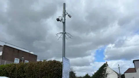 George Carden/BBC A metal pole with a sign saying private land and three cameras on it in the car park