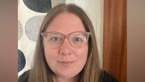 A woman with glasses poses for a selfie 