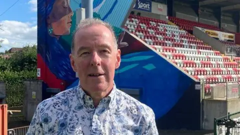 Man in blue patterned shirt standing in front of the new mural 