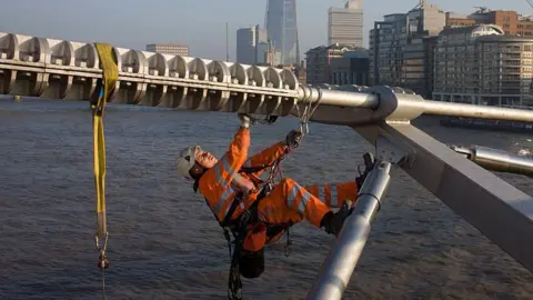 Getty Images A member of cleaning crew in orange high-viz clothing washes the Millennium Bridge.
