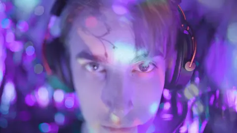 Face of a young man wearing a gaming headset, his face is lit in purple light
