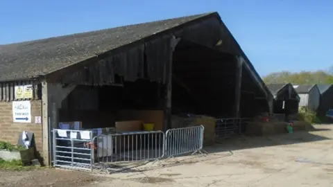 HSE A large brick-built barn at Hazelgrove Farm with metal barriers and bales of hay blocking one open side.