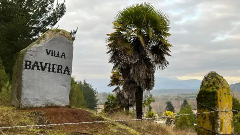 Grace Livingston Stone Painted White and With Words "Villa" means the way to settlement. In the foreground you can see the barbed wire fence as palm and mountains are in the background