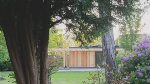 RIBA A timber building in the background, with trees and a lawn in the foreground