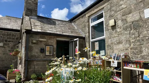 Beautiful old granite and slate school building with daisies in the front and library books and an open door