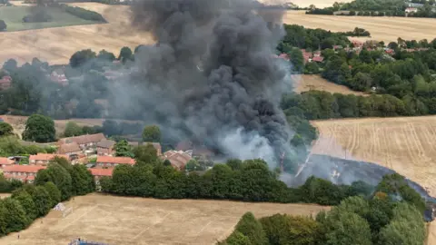 Lee Watson Plumes of black smoke can be seen rising from a field and engulfing nearby homes