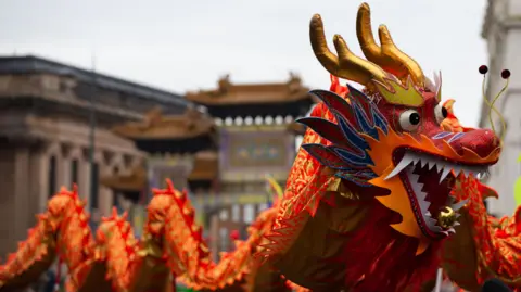 A red and gold chinese dragon parade takes place in Liverpool's Chinatown in front of the city's Chinese Arch