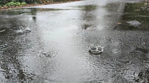 A road which is filled with standing water, you can see rain drops hitting the water.