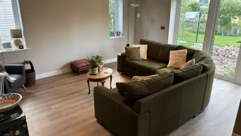 Luke Deal/BBC A living room area. There is a curved green sofa, blue single chair and a coffee table. To the rear of the room are French doors leading to a garden.