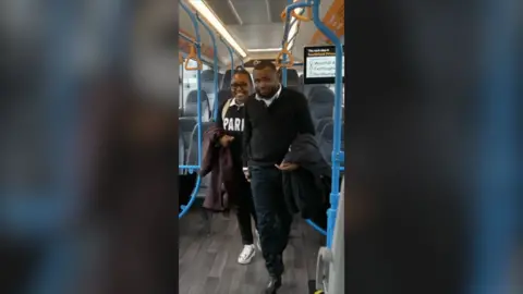 A man and a woman smile while walking through a bus