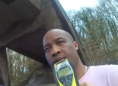 Vincent Lime on the side of the M4. He is attempting to do a road side breath test. The image is from a body worn camera.