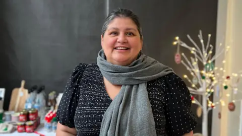 Chantal Rautenbach pictured smiling at the camera. She has dark black and grey hair tied back. She is wearing a grey scarf and black dress with white polka dots.