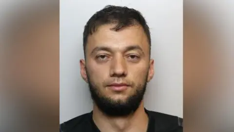 A mugshot of Nistor, who has short, dark hair and is wearing a dark top. Only his head and shoulders are visible. 