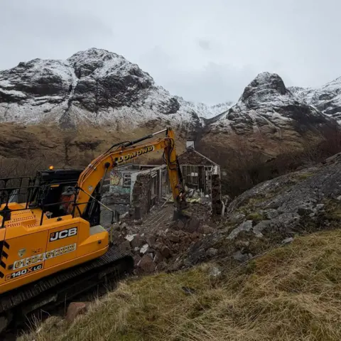 Harris Aslam family An orange excavator breaks down walls of the property. The mountains beyond are dusted with snow.