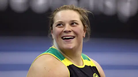 Sophie McKinna looking upwards to the left. She is smiling. The picture has been taken during a shot put competition.