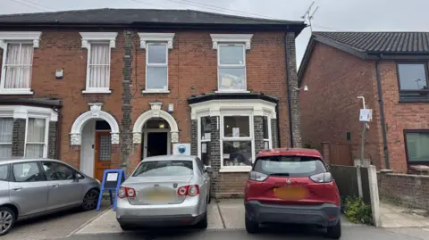 George King/BBC A view of the animal centre from the road. It looks like a terraced house and two cars are parked on its driveway.