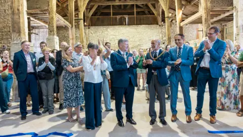National Trust A crowd of people have gathered inside Gawthorpe Hall to celebrate the opening. They are all smiling and clapping.