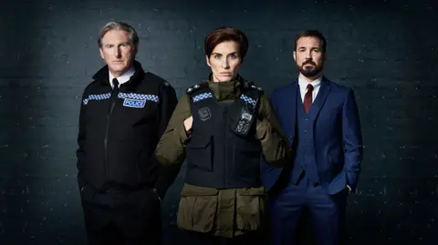Line of Duty characters Ted, Kate and Steve pose together. Ted and Kate wear police uniforms, while Steve wears a blue suit