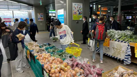 Menschen wurden gesehen, wie sie Produkte an einem Lebensmittelkiosk am Bahnhof Urawa in Japan untersuchten