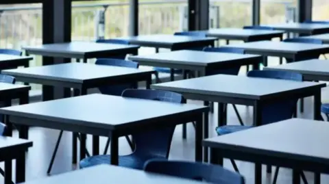 Getty Images A number of empty school desks in a classroom.