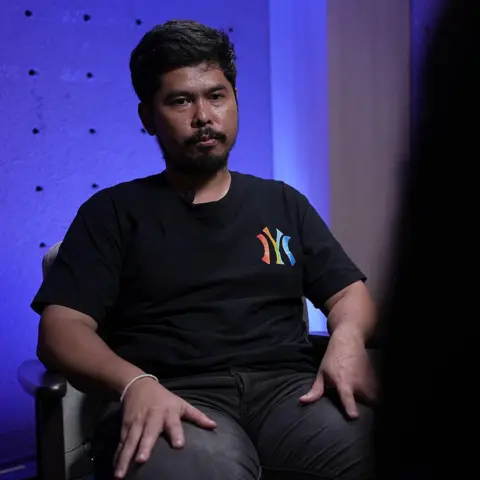 BBC Thai/Wasawat Lukharang Guitarist Chanate Trasing, in a black T-shirt and black pants, sits during an interview with BBC Thai