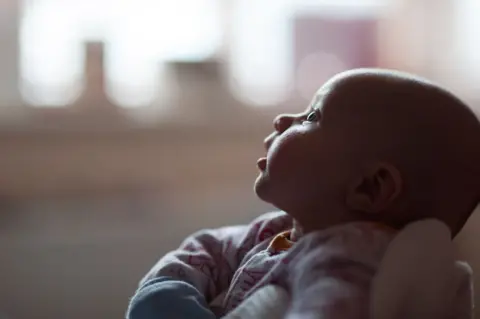 Side profile image of a six-week-old baby gazing at her mother, off frame.