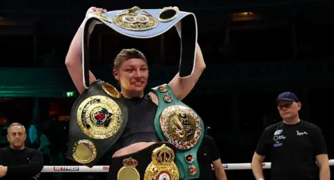 Lauren Price holds her world title belts in the ring
