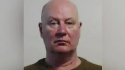 The mug shot of a bald white man with a ruddy face.