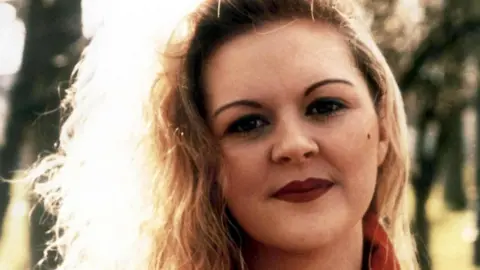Close shot of a woman with blonde curly hair, she is wearing red lipstick and a red top