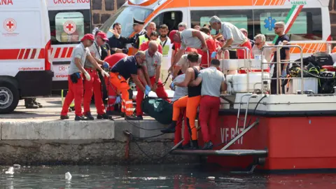 Hulpdiensten dragen een lijkzak nadat een zeilboot maandagochtend vroeg in de vroege uren van Porticello, nabij de Siciliaanse stad Palermo, Italië, op 19 augustus 2024 is gezonken.