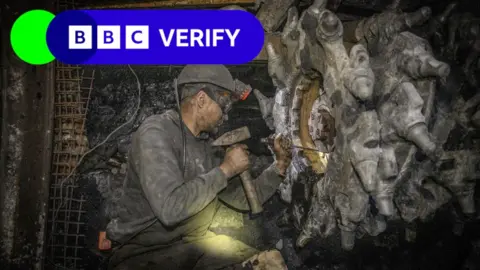 Man underground mining. He has a hat with a light on it. BBC Verify branding is written in the top left of the image.