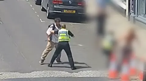 Wiltshire Police A video shot of PC Crabbe from behind in the middle of a road with her hand out to try and push a man away.