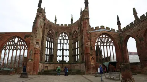 Reuters Cathedral ruins on a cloudy day. The ruins have high walls and ornate window frames still intact, but no roof.