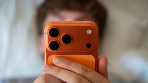 A teenage boy is pictured staring into a phone, suggesting he is using social media.