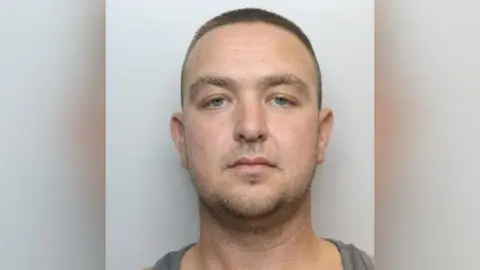 South Yorkshire Police A police photograph of Hooley, who has shaven brown hair and facial stubble. He has blue eyes and is wearing a grey top.