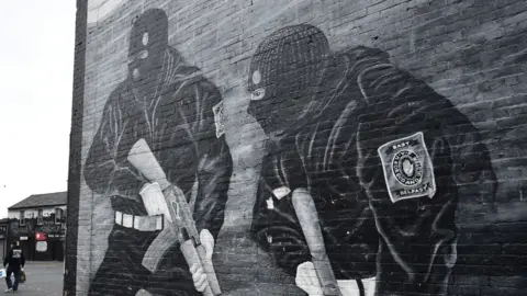 Getty Images Black and white mural of two paramilitary gunmen holding guns and wearing balaclavas on a wall in east Belfast