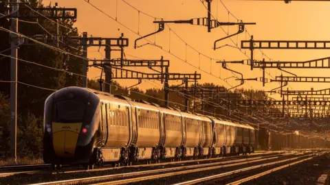 Steve Franklin An eight-carriage train in Grove sits in an orange glow created by a low-lying sun and surrounded by overhead power cables