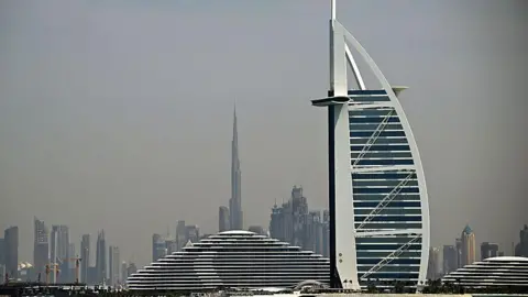 AFP via Getty Images Buildings on the Dubai skyline, with tall towers seen in the background and the sail-shaped hotel the Burj Al Arab in the foreground, against a grey sky 